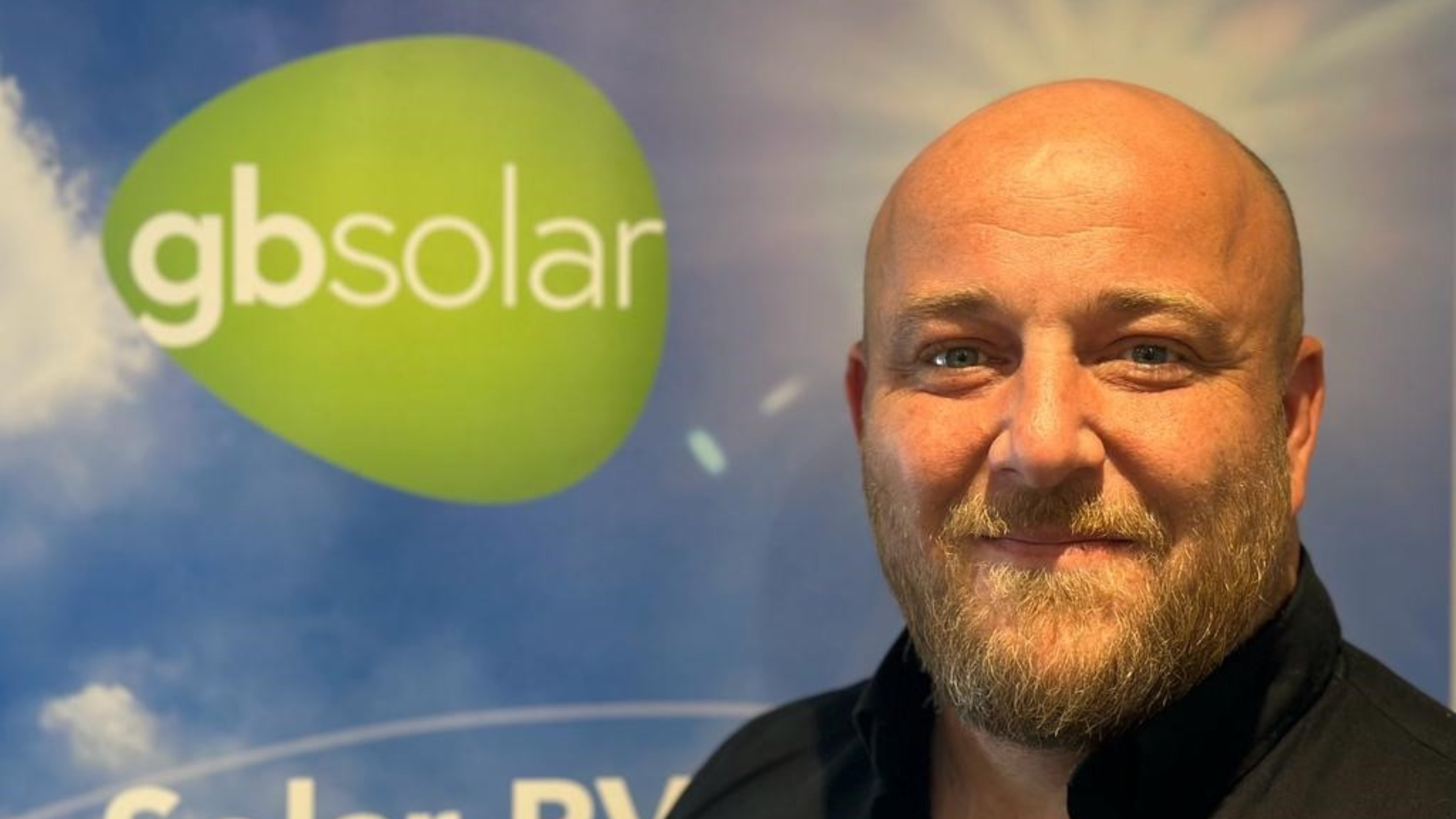 Man with beard looking at camera in front of GB Solar branded banner